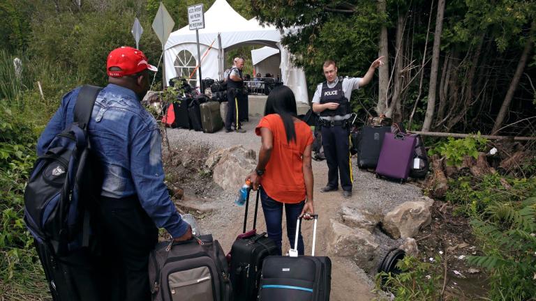In this Aug. 7, 2017 file photo, a Royal Canadian Mounted Police officer informs a migrant couple of the location of a legal border station, shortly before they illegally crossed from Champlain, N.Y., to Saint-Bernard-de-Lacolle, Quebec, using Roxham Road. (AP Photo / Charles Krupa, File)