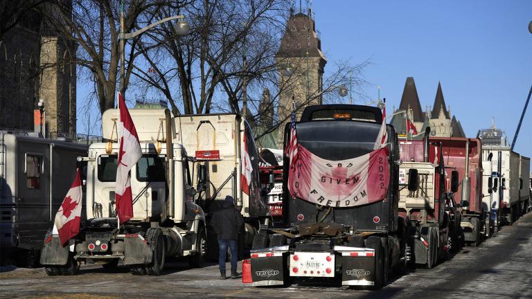 A person walks among trucks as Wellington Street is lined with trucks once again after city officials negotiated to move some trucks towards Parliament and away from downtown residences, on the 18th day of a protest against COVID-19 measures that has grown into a broader anti-government protest, in Ottawa, on Monday, Feb. 14, 2022. (Justin Tang / The Canadian Press via AP)