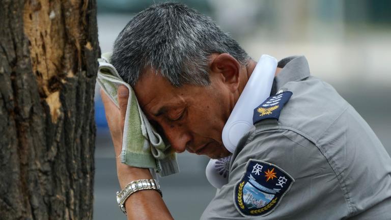 A security guard wearing an electric fan on his neck wipes his sweat on a hot day in Beijing, Monday, July 3, 2023. (AP Photo / Andy Wong)
