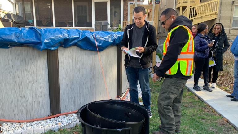 Resident Marco Moran, 33, speaks with Streets and Sanitation Ward Superintendent Carlos Cintron on Nov. 12, 2024, as he receives a free backyard compost bin on behalf of his sister, who owns the Galewood residence on the Northwest Side. (Eunice Alpasan / WTTW News)