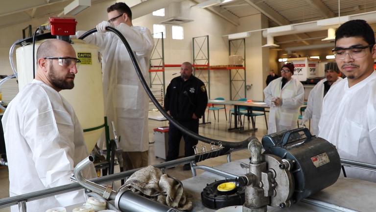 Cook County Jail inmate Harris Coteus, standing, fills the biodiesel processor with used vegetable oil from the jail’s officer dining hall. (Evan Garcia / WTTW News)
