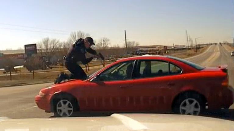 In this image taken from police dash cam video and released by the Carroll County Attorney, Carroll police Officer Patrick McCarty points his pistol at Dennis James Guider Jr. as Guider flees with McCarty on the hood of the vehicle after a traffic stop on March 5, 2021, in Carroll, Iowa. (Carroll County Attorney via AP)