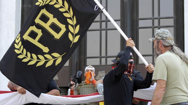 In this Sept. 7, 2020 photo, a protester carries a Proud Boys banner, symbol of a right-wing group, while other members start to unfurl a large U.S. flag in front of the Oregon State Capitol in Salem, Ore. (AP Photo / Andrew Selsky, File)