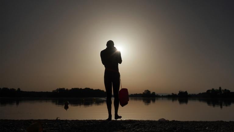 FILE - A man prepares to enter the water as the sun rises above the Miribel lake, outside Lyon, France, June 18, 2022. (Laurent Cipriani / AP Photo, File)