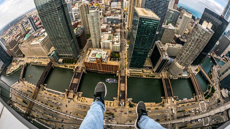 A self-described “rooftopper” dangles his feet, a familiar perspective for such photographers, while sitting atop a Chicago skyscraper. (Courtesy Andrew Fitzsimmons)