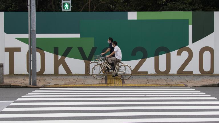 In this July 1, 2021, file photo, men cycle along the wall installed to close off a park being prepared for the Olympics and Paralympics Games in Tokyo. (AP Photo / Hiro Komae, File)