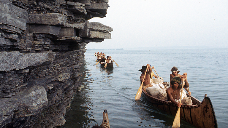 Paddling past a limestone spire on Lake Ontario, August 26, 1976. The canoe at the front contains Rich Gross, Bob Kulick, Reid Lewis, and John DiFulvio. (Photographers of the La Salle: Expedition II).