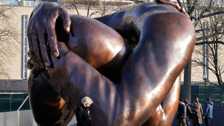 Passers-by walk near the 20-foot-high bronze sculpture "The Embrace," a memorial to Dr. Martin Luther King Jr. and Coretta Scott King, in the Boston Common, Tuesday, Jan. 10, 2023, in Boston. The sculpture, consisting of four intertwined arms, was inspired by a photo of the Kings embracing when MLK learned he had won the Nobel Peace Prize in 1964. The statue is to be unveiled during ceremonies Friday, Jan. 13, 2023. (AP Photo/Steven Senne)