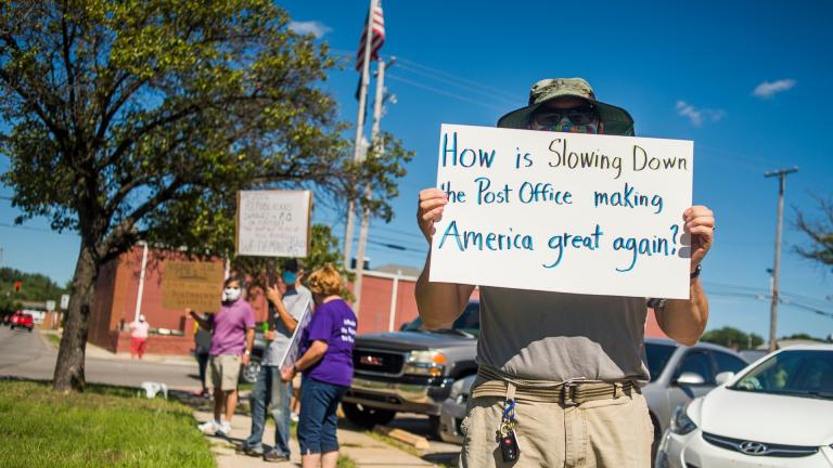 Eric Severson holds a sign as a few dozen people gather in front of the United States Post Office on Rodd St. to protest recent changes to the U.S. Postal Service under new Postmaster General Louis DeJoy on Tuesday, Aug. 11, 2020 in Midland, Mich. (Katy Kildee / Midland Daily News via AP)