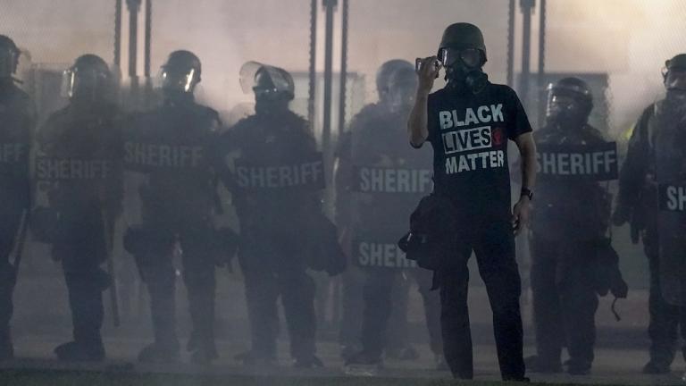 In this Aug. 25, 2020 file photo, a protester holds up a phone as he stands in front of authorities in Kenosha, Wis. (AP Photo/Morry Gash, File)