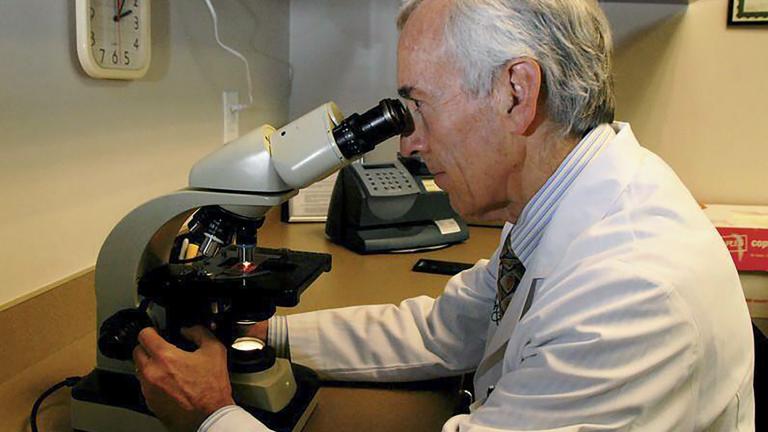 In this undated photo provided by Atlanta Allergy & Asthma, Dr. Stanley Fineman looks through a microscope at Atlanta Allergy & Asthma Center in Atlanta to examine pollen. (Robin B. Panethere / Atlanta Allergy & Asthma via AP)