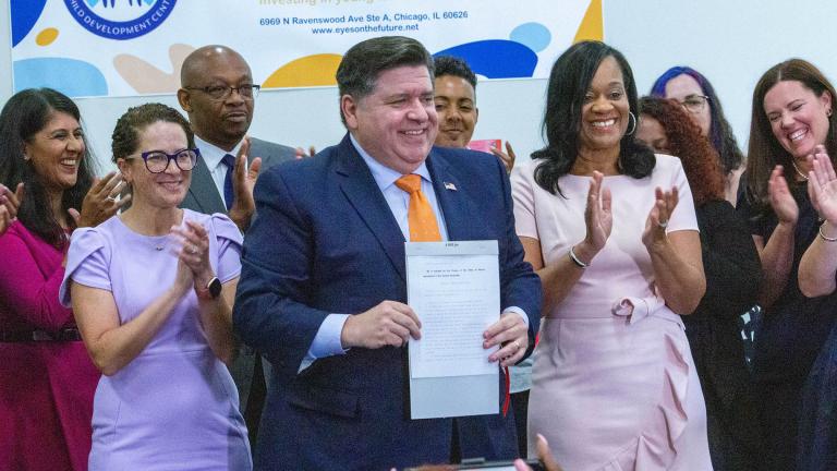 Gov. J.B. Pritzker holds up Senate Bill 1 after signing it into law, alongside various members of the Illinois General Assembly. He said the new state agency created by the law is expected to be up and running by 2026. (Dilpreet Raju / Capitol News Illinois)