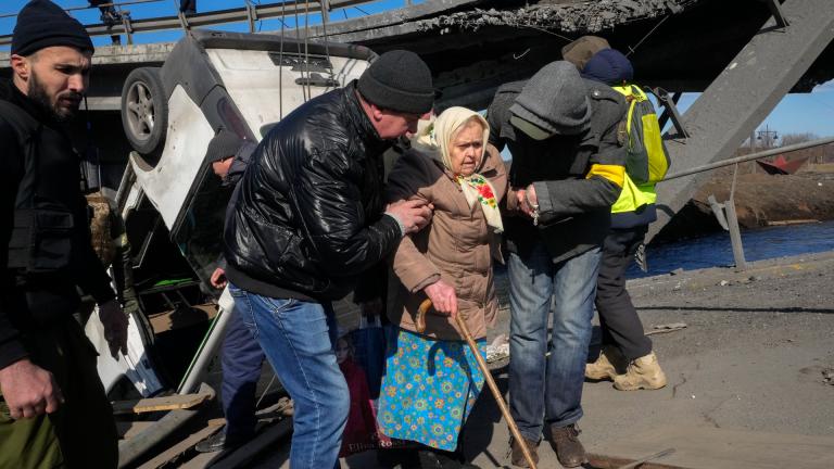 Volunteers pass an improvised path under a destroyed bridge as they evacuate an elderly resident in Irpin, some 25 km (16 miles) northwest of Kyiv, Friday, March 11, 2022. Kyiv northwest suburbs such as Irpin and Bucha have been enduring Russian shellfire and bombardments for over a week prompting residents to leave their home. (AP Photo / Efrem Lukatsky)