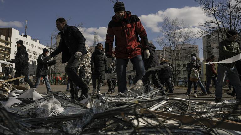 People clear debris outside a medical center damaged after parts of a Russian missile, shot down by Ukrainian air defense, landed on a nearby apartment block, according to authorities, in Kyiv, Ukraine, Thursday, March 17, 2022. (AP Photo / Vadim Ghirda)