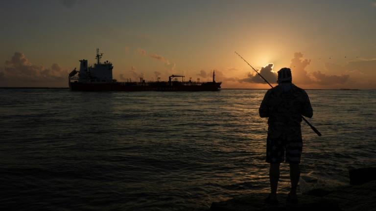 An oil tanker passes at sunrise while a man fishes in Port Aransas, Texas, Aug. 9, 2025. (AP Photo / Eric Gay, File)