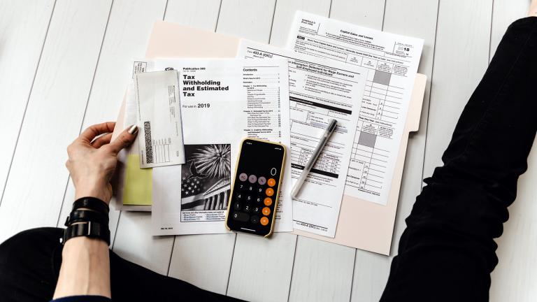 Person holding paper near pen and calculator. (Kelly Sikkema / Unsplash)
