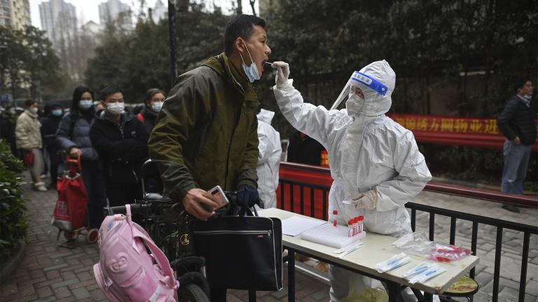 A man holding his bicycle with a school bag on it gets a throat swab during a mass COVID-19 test at a residential compound in Wuhan in central China's Hubei province, Tuesday, Feb. 22, 2022. (Chinatopix via AP)