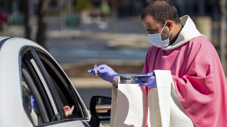 In this Sunday, March 22, 2020 file photo, the Rev. William A. Mentz, pastor of the Scranton, Pa.-based St. Francis and Clare Progressive Catholic Church, wears a mask and gloves while distributing prepackaged communion to the faithful attending Mass while sitting in their cars in the parking lot of a shopping center in Moosic, Pa. (Christopher Dolan/The Times-Tribune via AP)