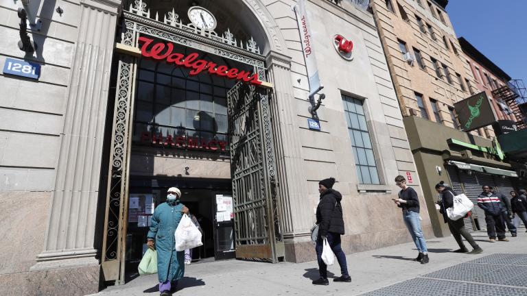 In this March 26, 2020 file photo, a woman leaves a Walgreens pharmacy that is enforcing social distancing rules by allowing only a certain numbers of people in as customers line up on the sidewalk outside the store in New York. The coronavirus pandemic pushed the drugstore chain to a $1.7-billion loss in its fiscal third quarter, as customers stayed home to avoid the virus or consolidated their shopping to grocery stores. (AP Photo/Kathy Willens, File)