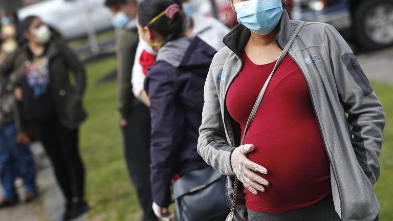 In this May 7, 2020 file photo, a pregnant woman wearing a face mask and gloves holds her belly as she waits in line for groceries at St. Mary’s Church in Waltham, Mass. (AP Photo / Charles Krupa, file)