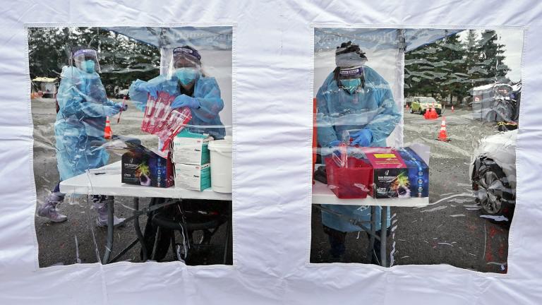 Workers at a drive-up COVID-19 testing clinic stand in a tent as they prepare PCR coronavirus tests, Jan. 4, 2022, in Puyallup, Wash., south of Seattle. (AP Photo / Ted S. Warren, File)