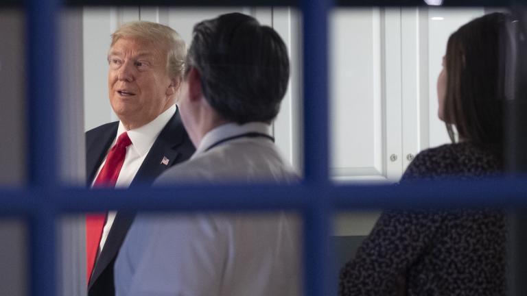 As seen through a window, President Donald Trump watches newscasts in an area behind the James Brady Press Briefing Room with Steven Groves, center, White House deputy press secretary, and press assistant Margo Martin, after speaking about the coronavirus at the White House, Friday, April 17, 2020, in Washington. (AP Photo/Alex Brandon)