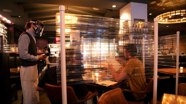 In this June 22, 2020, file photo, wearing a face shield, server Brandon Fricke, left, takes orders from dine-in customers surrounded by protective dividers at Water Grill seafood restaurant in Los Angeles. (AP Photo / Jae C. Hong, File)