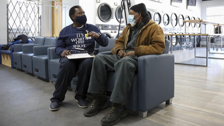 Herman Simmons, left, makes a vaccination appointment for Theopulis Polk, right, at a Chicago laundromat on Saturday, March 6, 2021. (AP Photo/Teresa Crawford)