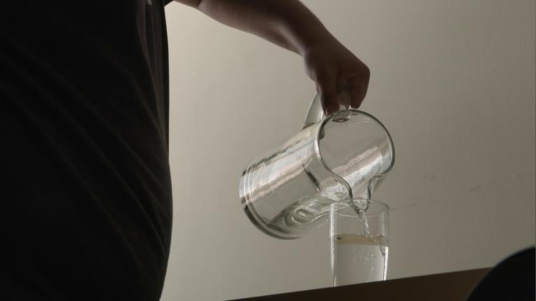 Someone pours a glass of water into a pitcher. (Medill)