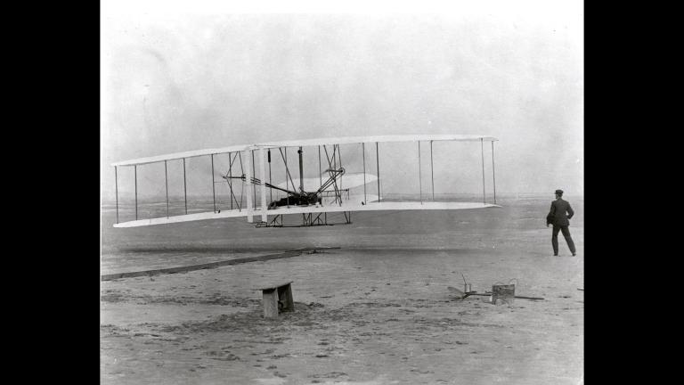 Orville Wright pilots a historic, 12-second flight on Dec. 17, 1903 at Kitty Hawk, North Carolina, as Wilbur Wright observes.