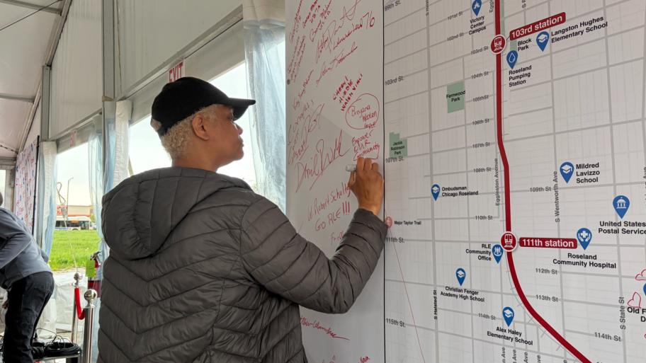 An attendee signs a poster during a Red Line extension project ceremonial groundbreaking event on April, 24, 2026, near Michigan Avenue and 116th Street, the future site of one of the new Red Line stations. (Eunice Alpasan / WTTW News)