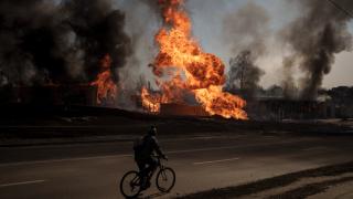 A man rides his bike past flames and smoke rising from a fire following a Russian attack in Kharkiv, Ukraine, March 25, 2022. (AP Photo / Felipe Dana, File)