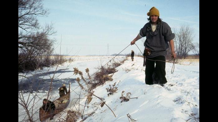 Mark Fredenburg tugs a canoe forward using a technique called "lining" on the banks of the Kankakee River. Below on the frozen river George LeSieutre and  Ken Lewis push the boat. January 1, 1977. (Photographers of the La Salle: Expedition II) 