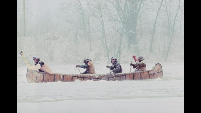 Trying to paddle down the half-frozen Kankakee River on January 5, 1977. At the front of the boat Doug Sohn uses an axe to chop through the ice while three men paddle through heavy snow behind him. (Photographers of the La Salle: Expedition II)