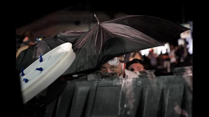 A protester takes cover during clashes outside the Kenosha County Courthouse late Tuesday, Aug. 25, 2020, in Kenosha, Wis., during a third night of unrest following the shooting of a Black man whose attorney said he was paralyzed after being shot multiple times by police. (AP Photo/David Goldman)