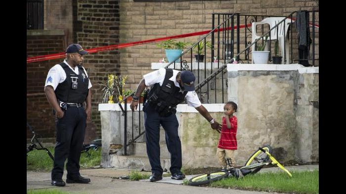 A Chicago police officer helps a child walk through an area being investigated after two men were shot Friday, July 3, 2020, in Chicago. (Ashlee Rezin Garcia / Chicago Sun-Times via AP)