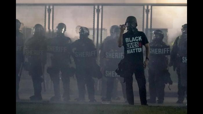 A protester holds up a phone as he stands in front of authorities Tuesday, Aug. 25, 2020, in Kenosha, Wis. (AP Photo / Morry Gash)