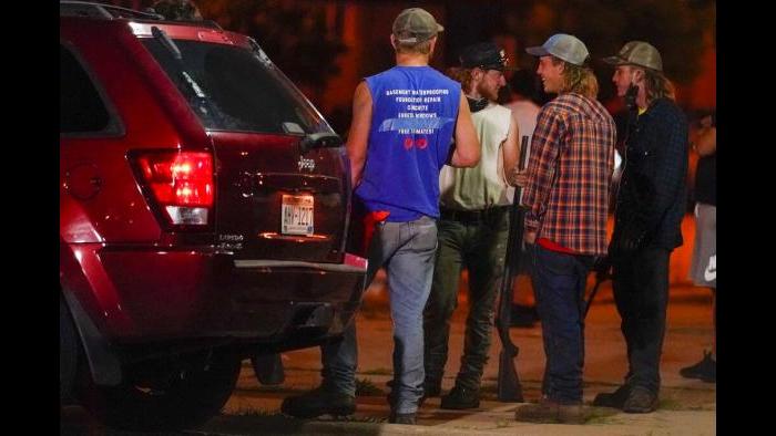 A group holds rifles as they watch protesters on the street Tuesday, Aug. 25, 2020, in Kenosha, Wis. Protests continued following the police shooting of Jacob Blake two days earlier. (AP Photo / Morry Gash)