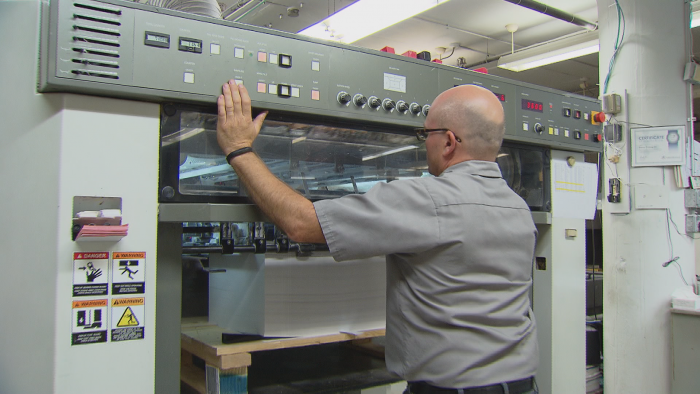 A pressman waits at the printing press for a job to finish.