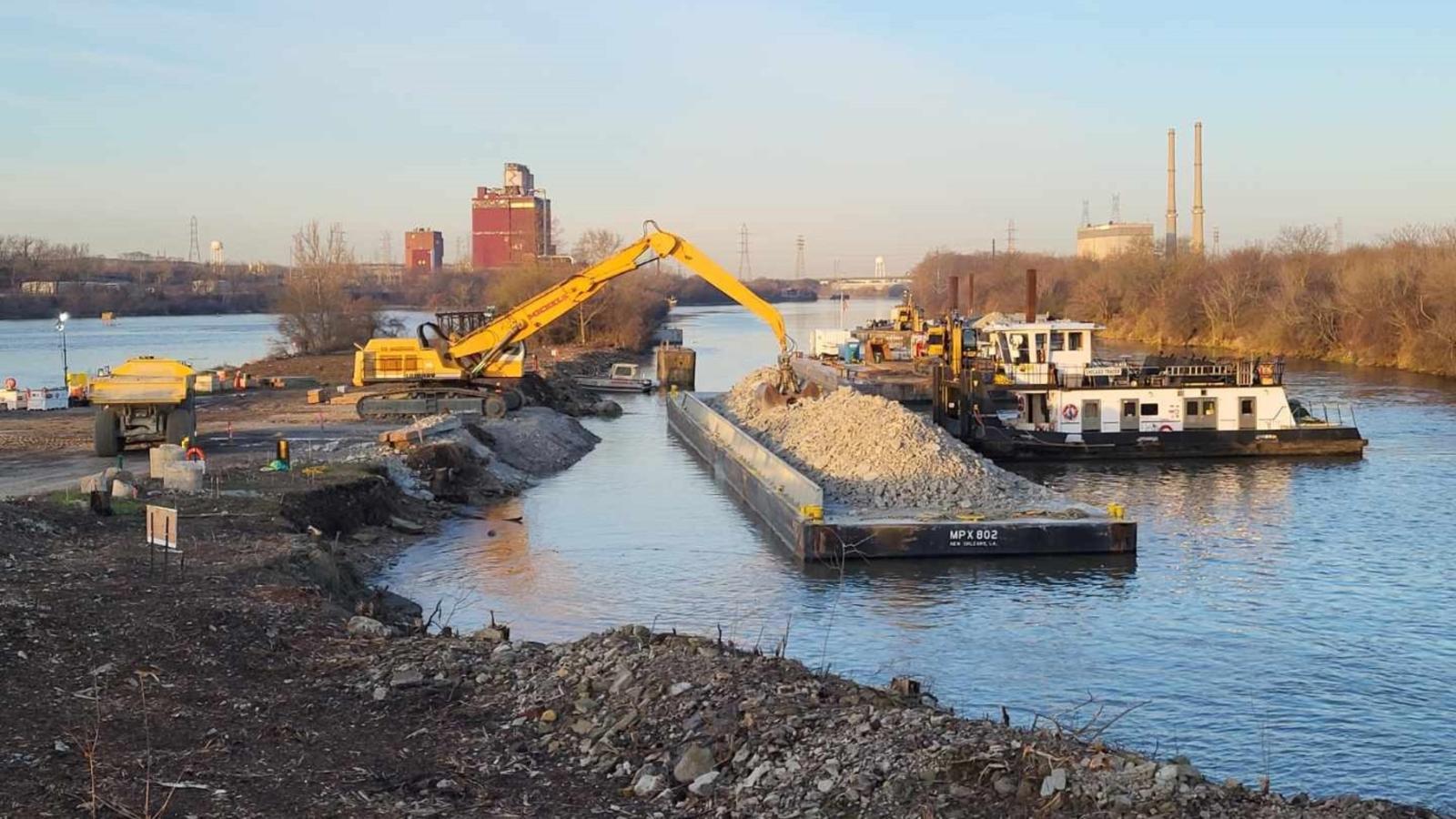 Rock which has been excavated from the river channel for construction of the Brandon Road Interbasin Project near Joliet, Illinois, is unloaded from a barge and placed into trucks for use in another area of the project. (U.S. Army Corps of Engineers)