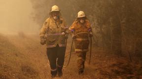 Firefighters drag their water hose after putting out a spot fire near Moruya, Australia, Saturday, Jan. 4, 2020. Australia’s Prime Minister Scott Morrison called up about 3,000 reservists as the threat of wildfires escalated Saturday in at least three states with two more deaths, and strong winds and high temperatures were forecast to bring flames to populated areas including the suburbs of Sydney. (AP Photo / Rick Rycroft) Firefighters drag their water hose after putting out a spot fire near Moruya, Australia, Saturday, Jan. 4, 2020. Australia’s Prime Minister Scott Morrison called up about 3,000 reservists as the threat of wildfires escalated Saturday in at least three states with two more deaths, and strong winds and high temperatures were forecast to bring flames to populated areas including the suburbs of Sydney. (AP Photo / Rick Rycroft)