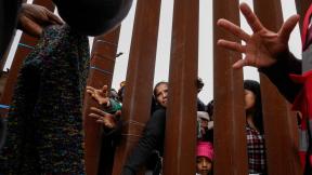Migrants reach through a border wall for clothing handed out by volunteers as they wait between two border walls to apply for asylum on May 12, 2023, in San Diego. (AP Photo / Gregory Bull, File)