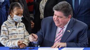 Gov. J.B. Pritzker signs an executive order March 18, 2024, alongside 7-year-old Kioko Jenkins, who has sickle cell disease, at La Rabida Children’s Hospital in Chicago. The order creates an advisory council to investigate how Illinois’ Medicaid program can help cover costs of emerging gene therapies. (Dilpreet Raju / Capitol News Illinois)