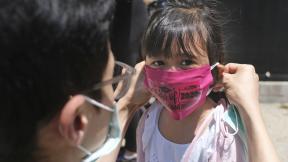 In this June 10, 2020, file photo, Olivia Chan’s father helps her with a new mask she received during a graduation ceremony for her Pre-K class in front of Bradford School in Jersey City, N.J. (AP Photo / Seth Wenig, File) In this June 10, 2020, file photo, Olivia Chan’s father helps her with a new mask she received during a graduation ceremony for her Pre-K class in front of Bradford School in Jersey City, N.J. (AP Photo / Seth Wenig, File)